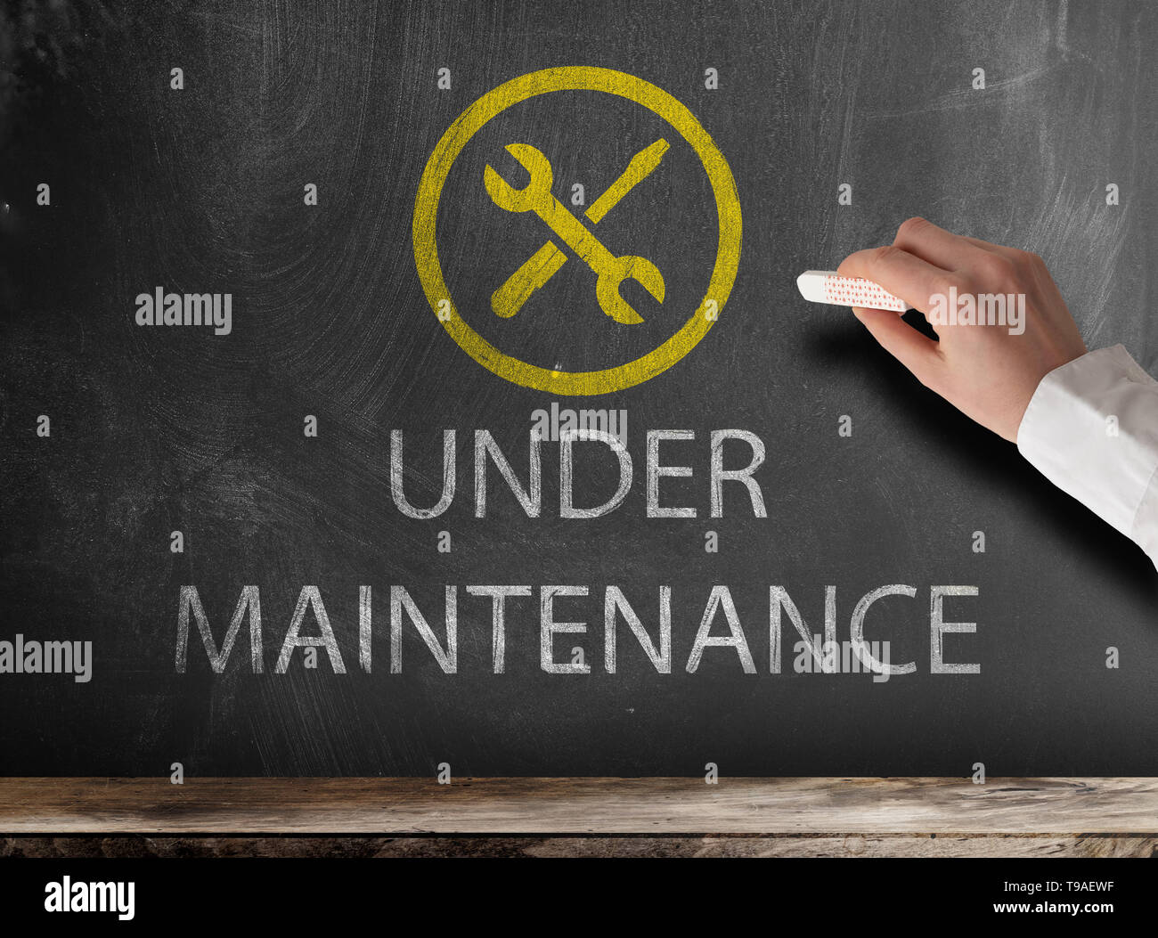 text UNDER MAINTENANCE and icon on chalkboard with hand holding piece of chalk Stock Photo