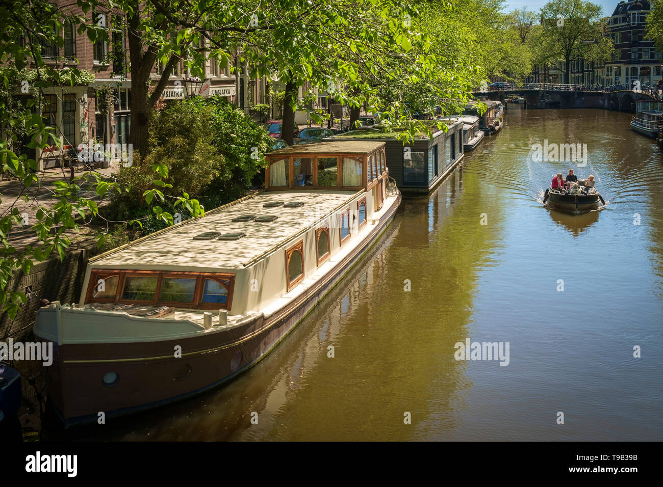 Houseboats and a pleasure boat on a sunny Amsterdam canal. Stock Photo