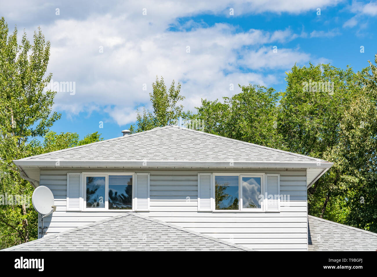 Top of residential house with satellite dish on side on cloudy sky