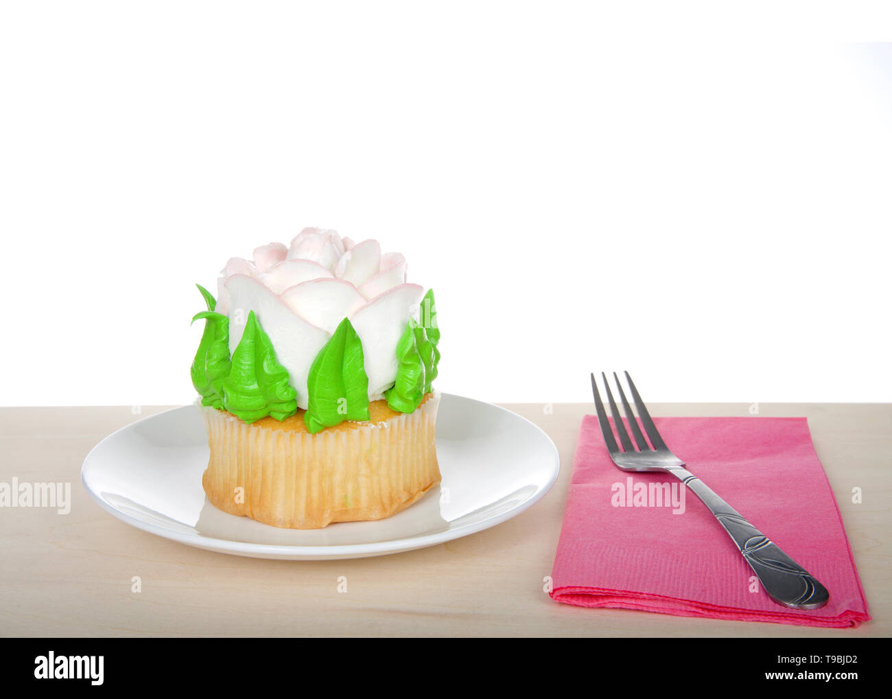 Large cup cake with giant frosting rose sitting on white plate on wood table, pink napkin with fork. Simple design with copy space for Mother's Day, V Stock Photo