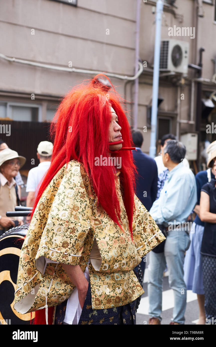 Japanese man in vibrant red wig and chin straps dressed as oni (ogre