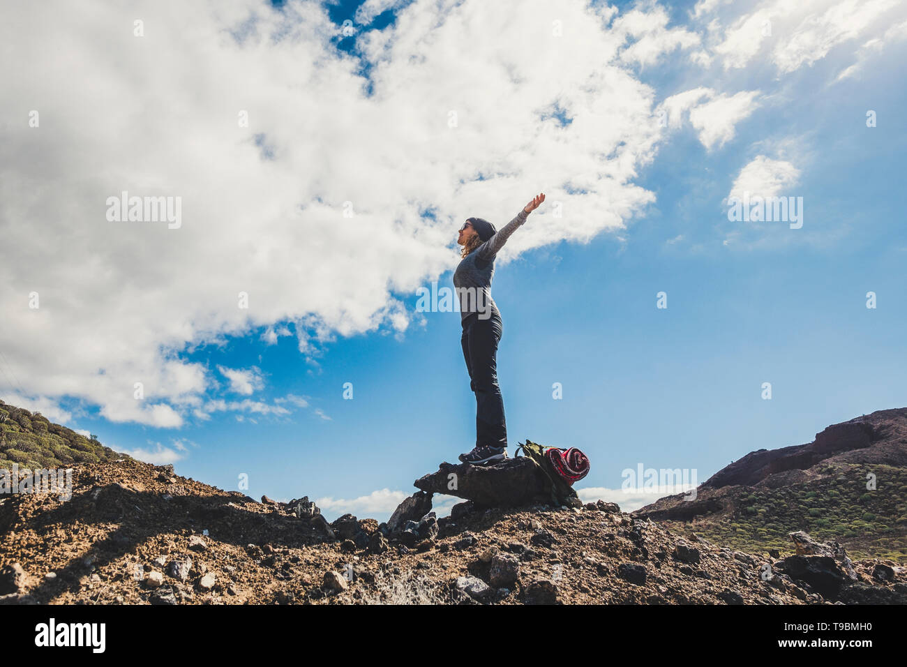 Happiness and freedom people concept - standing woman with backpack and adventure equipment opeing arms enjoying the outdoor nature around - success h Stock Photo