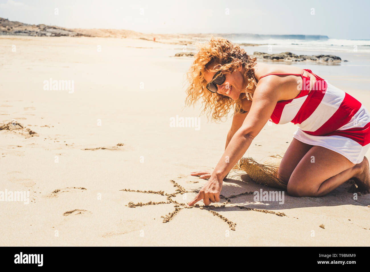 Happy cheerful woman on summer holiday vacation enjoying the beach and the outdoor designing a sun on the sand - beautiful curly caucasian people lady Stock Photo