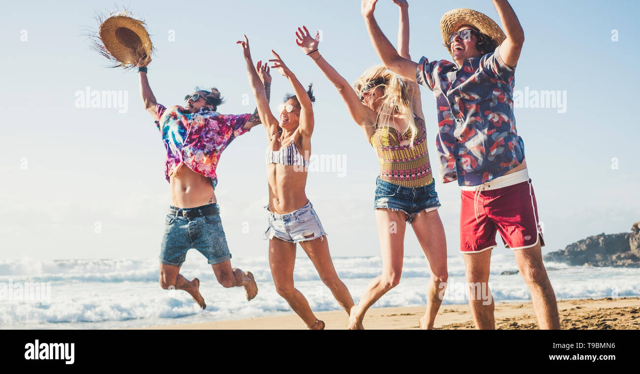 Happy group of young millennial active people jumping for fun at the beach on summer holiday vacation - travel and tourist concept with men and women  Stock Photo