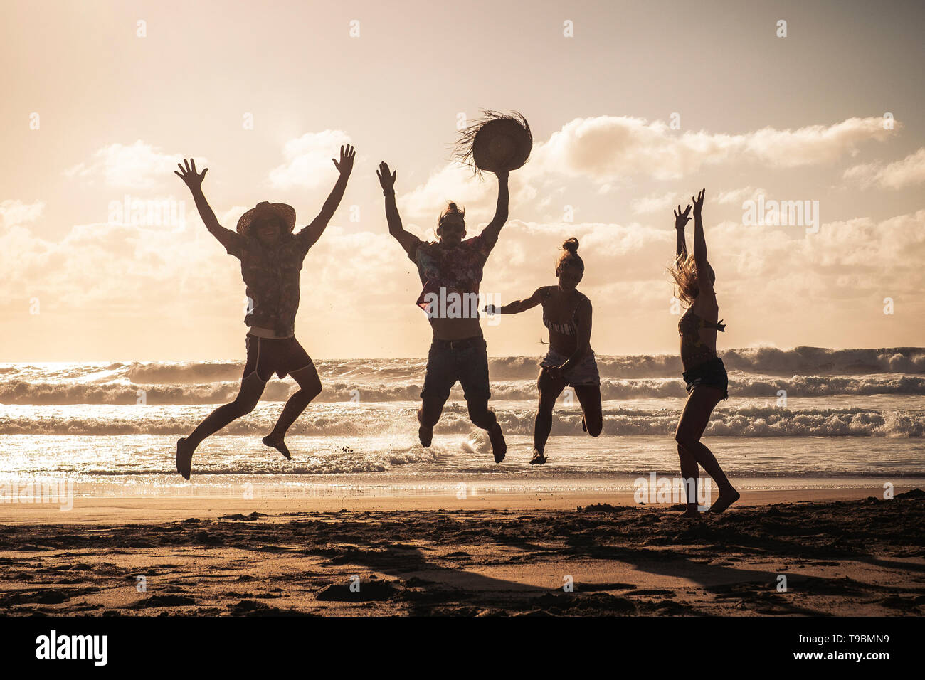 Sunset at the beach with happy group of young people jumping having fun ...