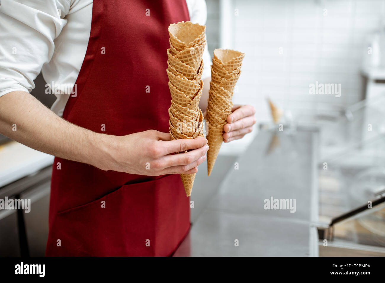 Man in red apron holding waffle cones selling ice cream in the shop