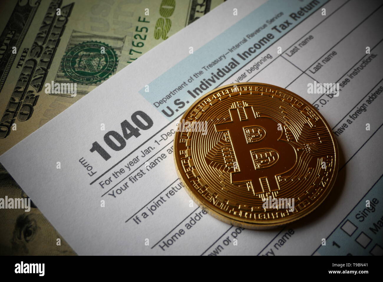 An golden Bitcoin, an virtual currency in physical coin form, displayed with the US 1040 Tax form, symbolic illustration for the taxation of bitcoin Stock Photo
