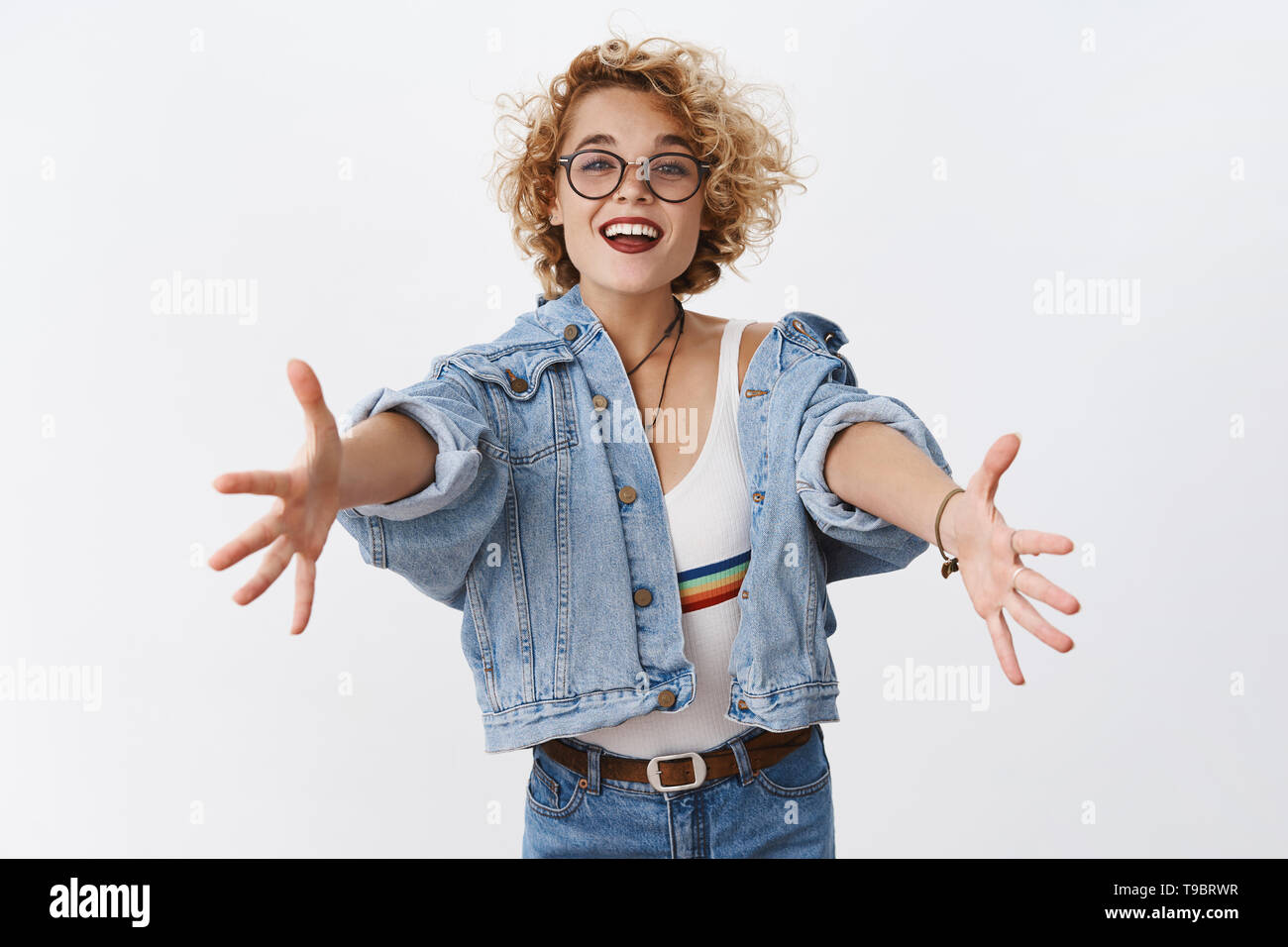 Outdoor fashion portrait of stylish young woman having fun, emotional face  , laughing, looking at camera. Urban city street style. Long jeans coat and  orange hoodie. Spring or fall outfit. Stock Photo