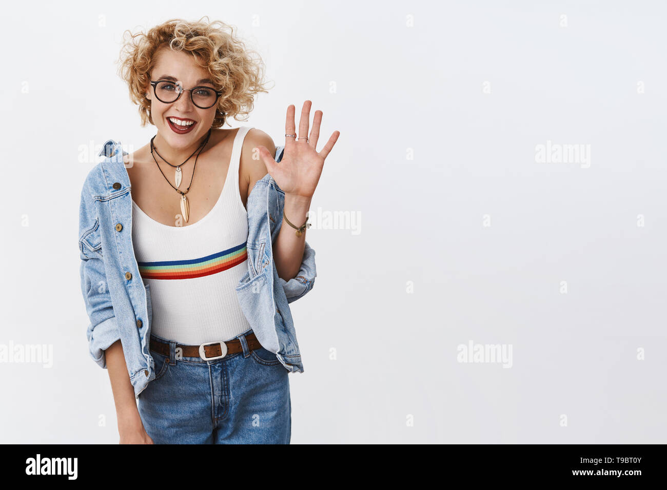 Five stars to your product. Indoor shot of enthusiastic stylish female blonde with glasses and pierced nose raising palm and smiling broadly giving Stock Photo