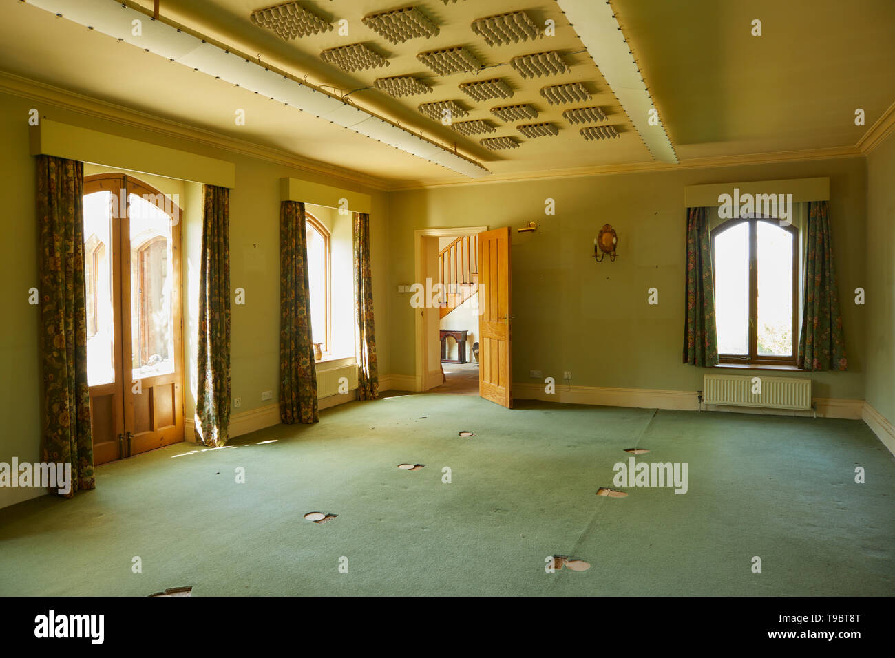 Once a billiard room a large carpeted empty area at the end of final house clearance. Sound deadening work to ceiling and flat lighting. Stock Photo