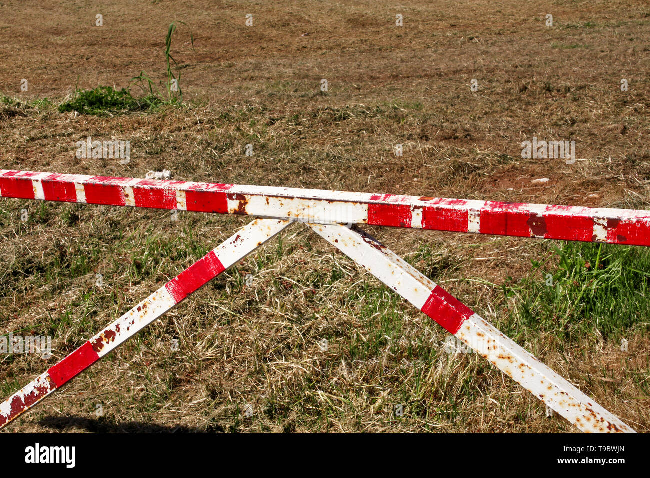 Red and white warning sign barrier on green grass in nature background. Transport, traffic regulation. Old fence made and white and red street parking Stock Photo