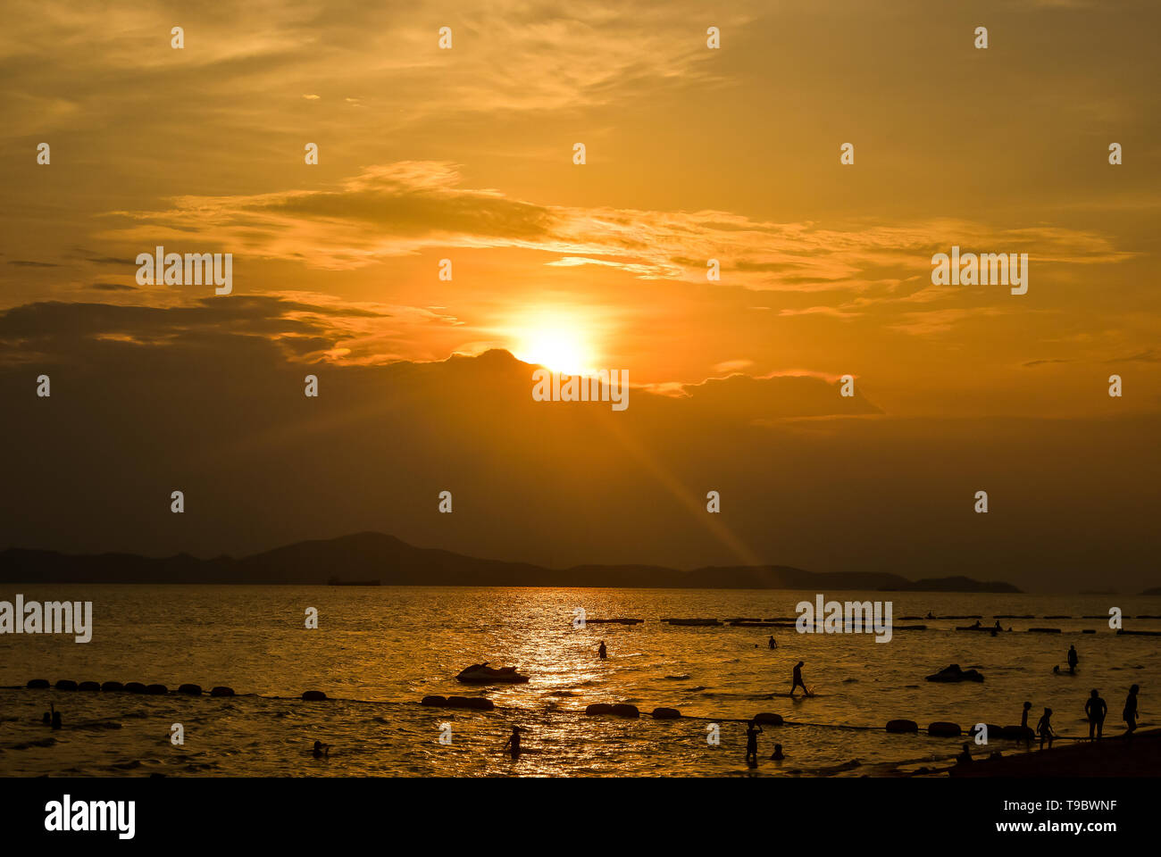 Beach sunset with silhouette people sandy on the tropical sea island summer colorful golden hour sky with sun over mountain background Stock Photo