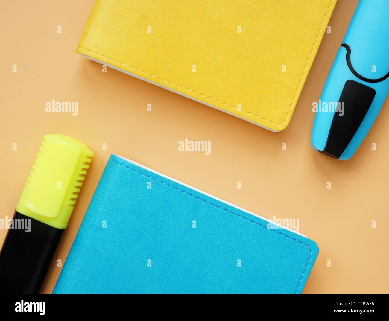 Top view of blue and yellow notepads and markers on an orange desk. Colorful office supply. Stock Photo