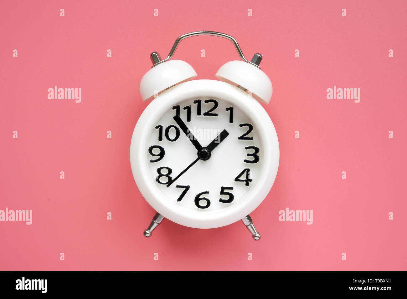 White alarm clock on a pink surface. Stock Photo