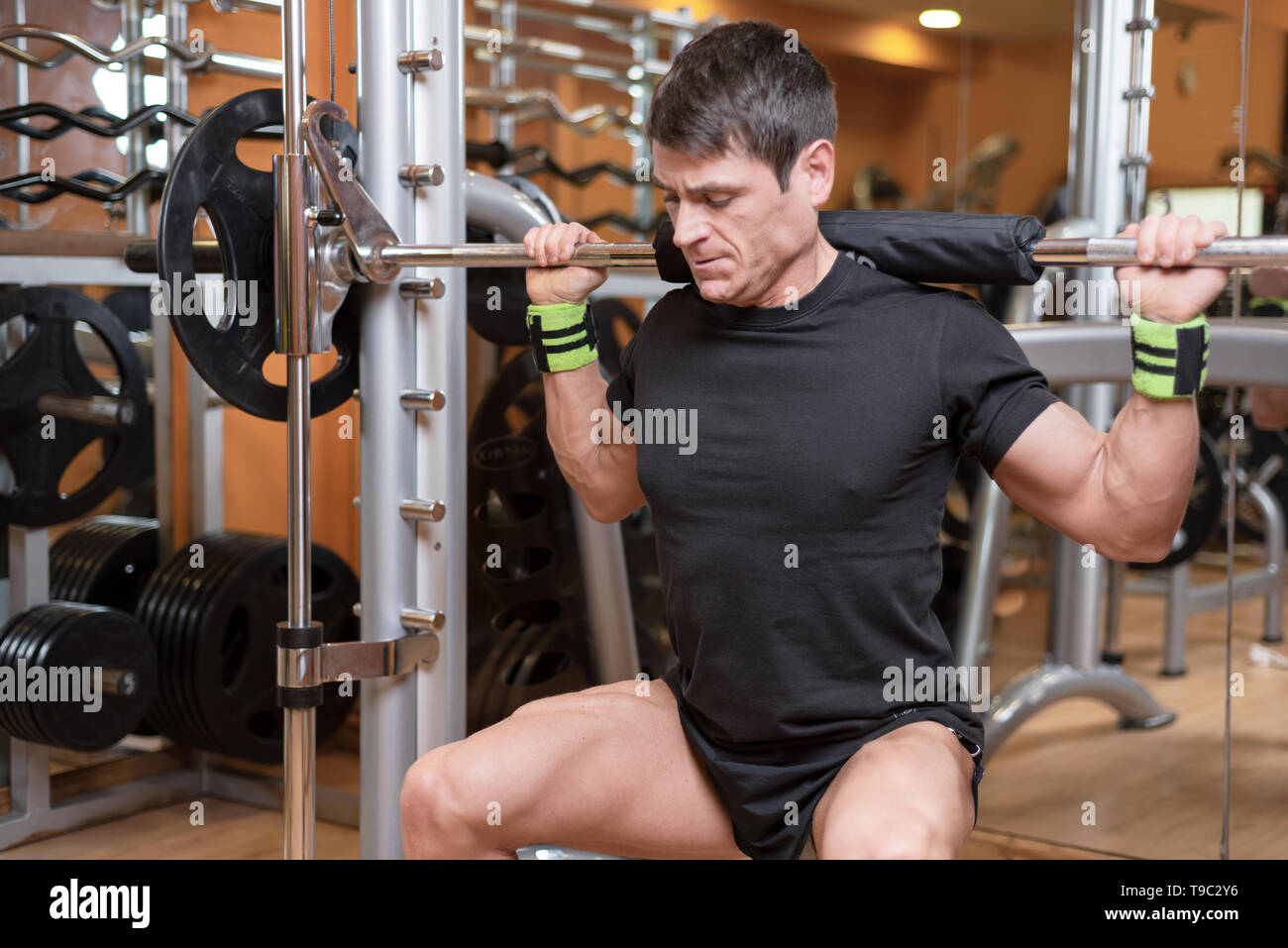 sport, bodybuilding, lifestyle and people concept - young man with barbell doing squats in gym . Stock Photo