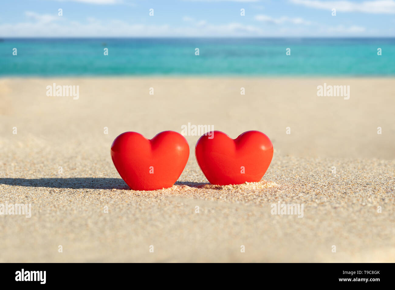 Close-up Of Two Red Heart Shape Dig On Sand At Beach Stock Photo