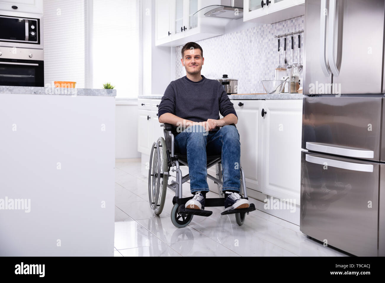 Smiling Young Handicapped Man Sitting On Wheelchair In Kitchen Stock Photo