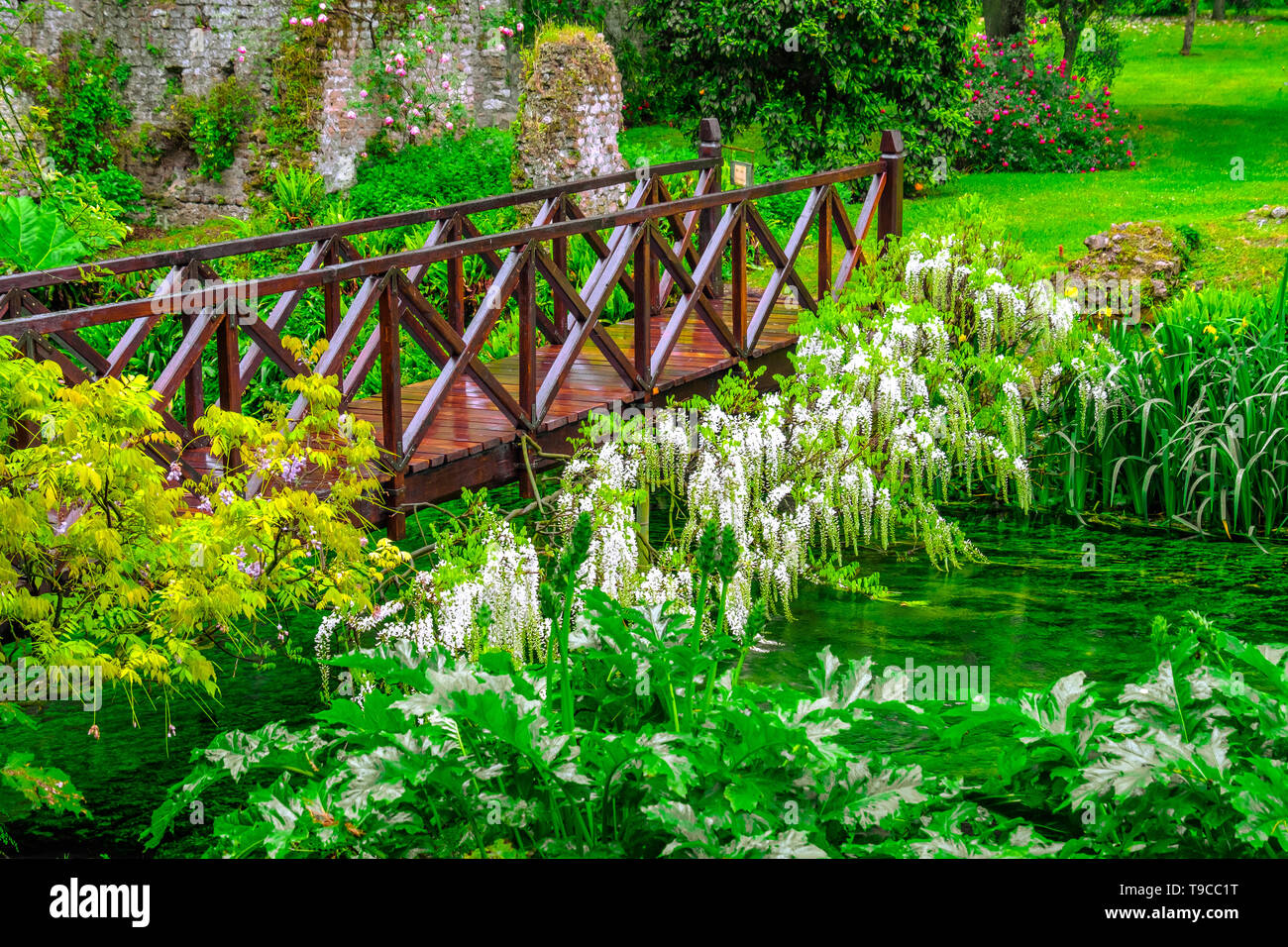 fairy tale bridge vivid green river wooden full of flowers in ornamental garden Stock Photo