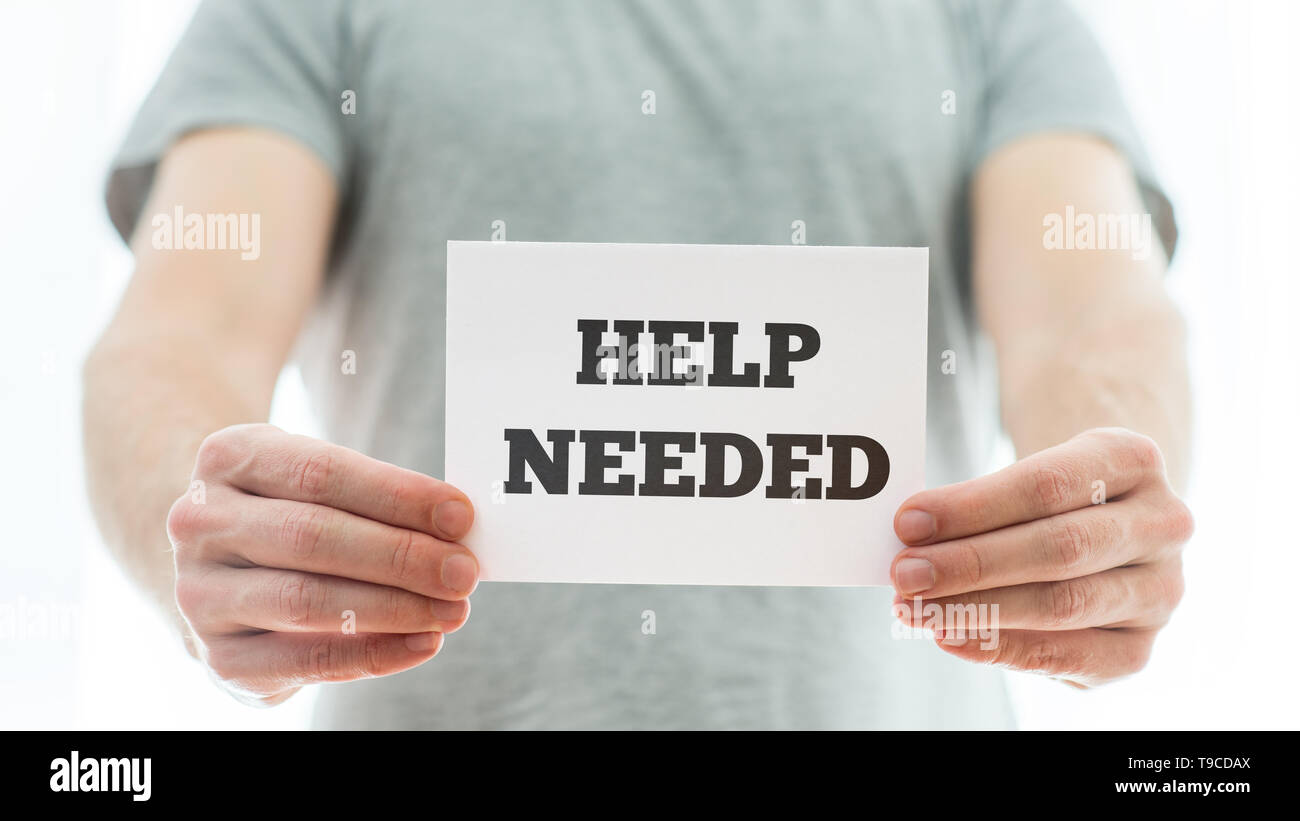 Man in a grey t-shirt holding a white card with Help needed sign representing a job offer or problematic of homeless people. Stock Photo