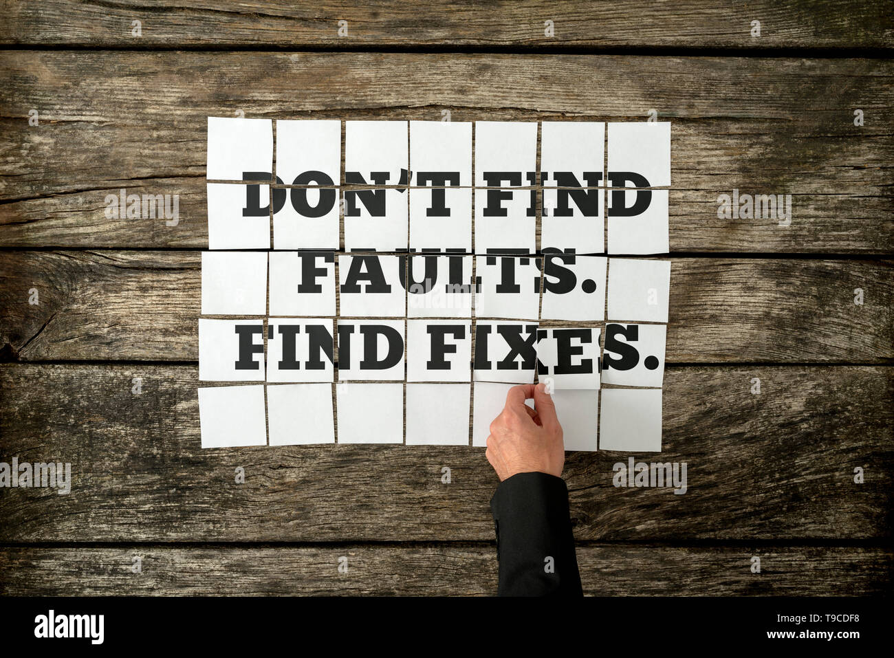 Top view of male hand assembling a Don't find faults. Find fixes sign with white cards over a textured rustic wooden boards. Stock Photo