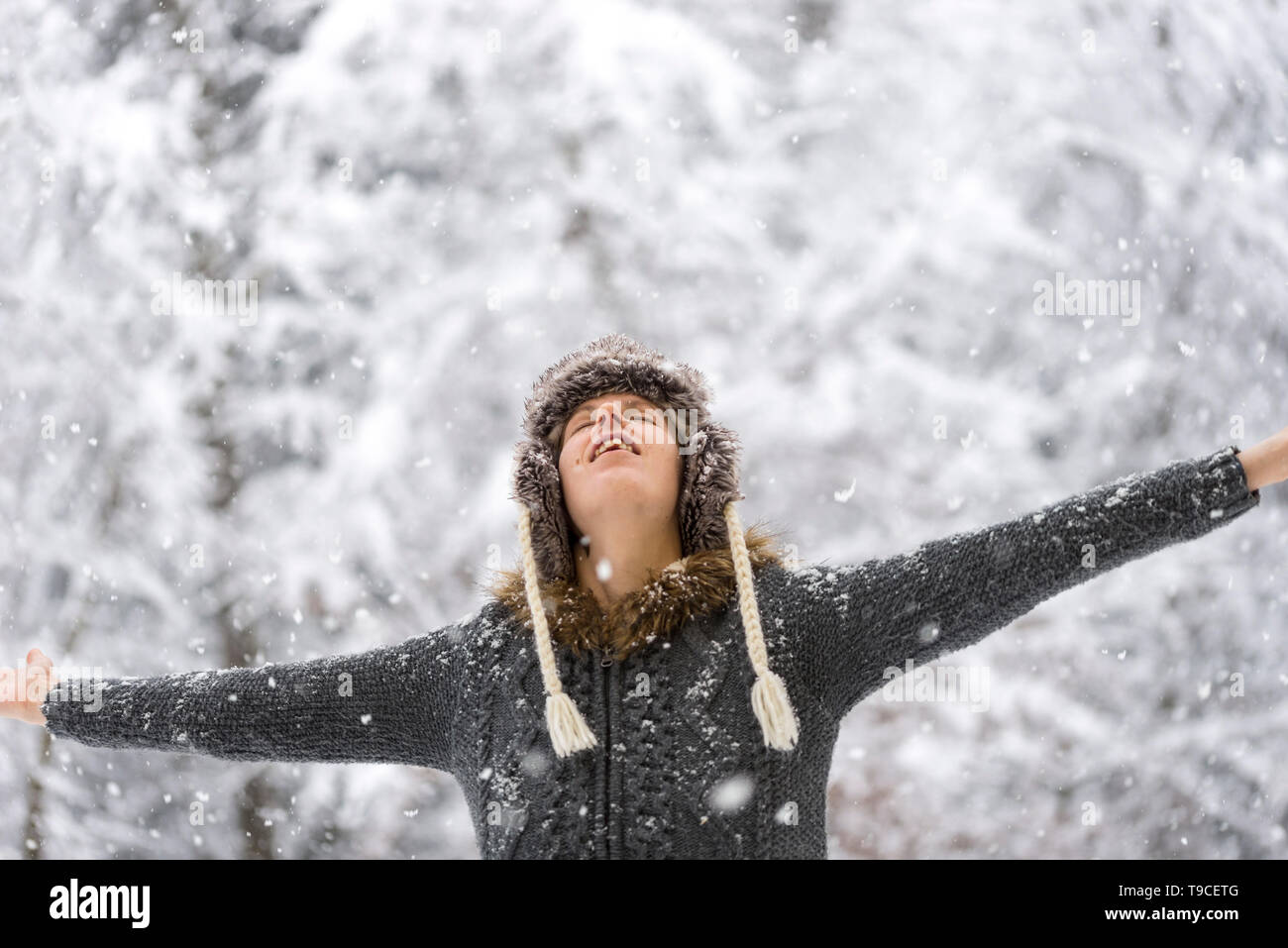 Woman standing outdoors in falling snow with her arms outspread and head tilted back with closed eyes. Stock Photo