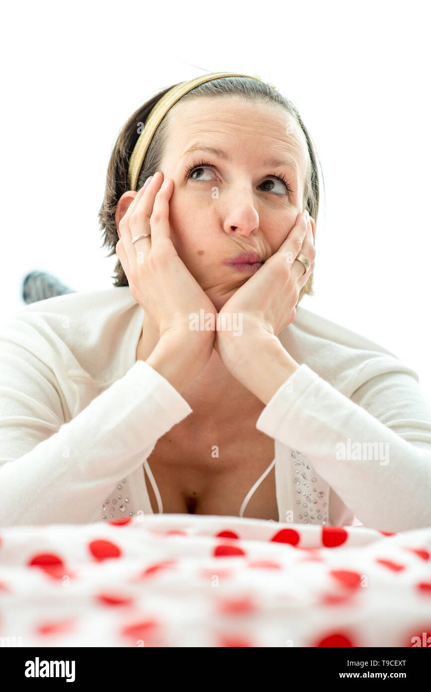 Young woman lying thinking on top of a colorful red polka dot counterpane on a bed looking up into the air with a contemplative expression. Stock Photo