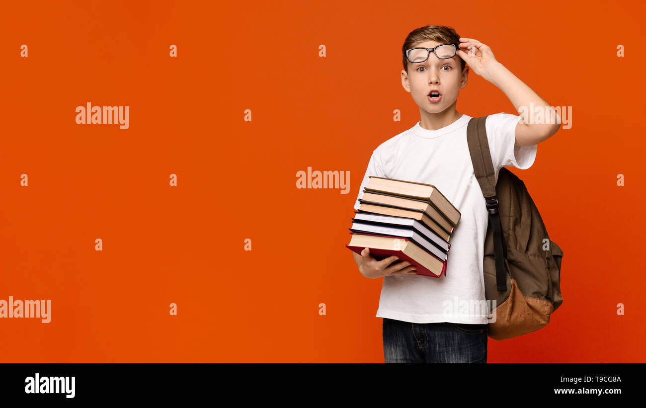 Shocked schoolboy in glasses holding stack of books Stock Photo