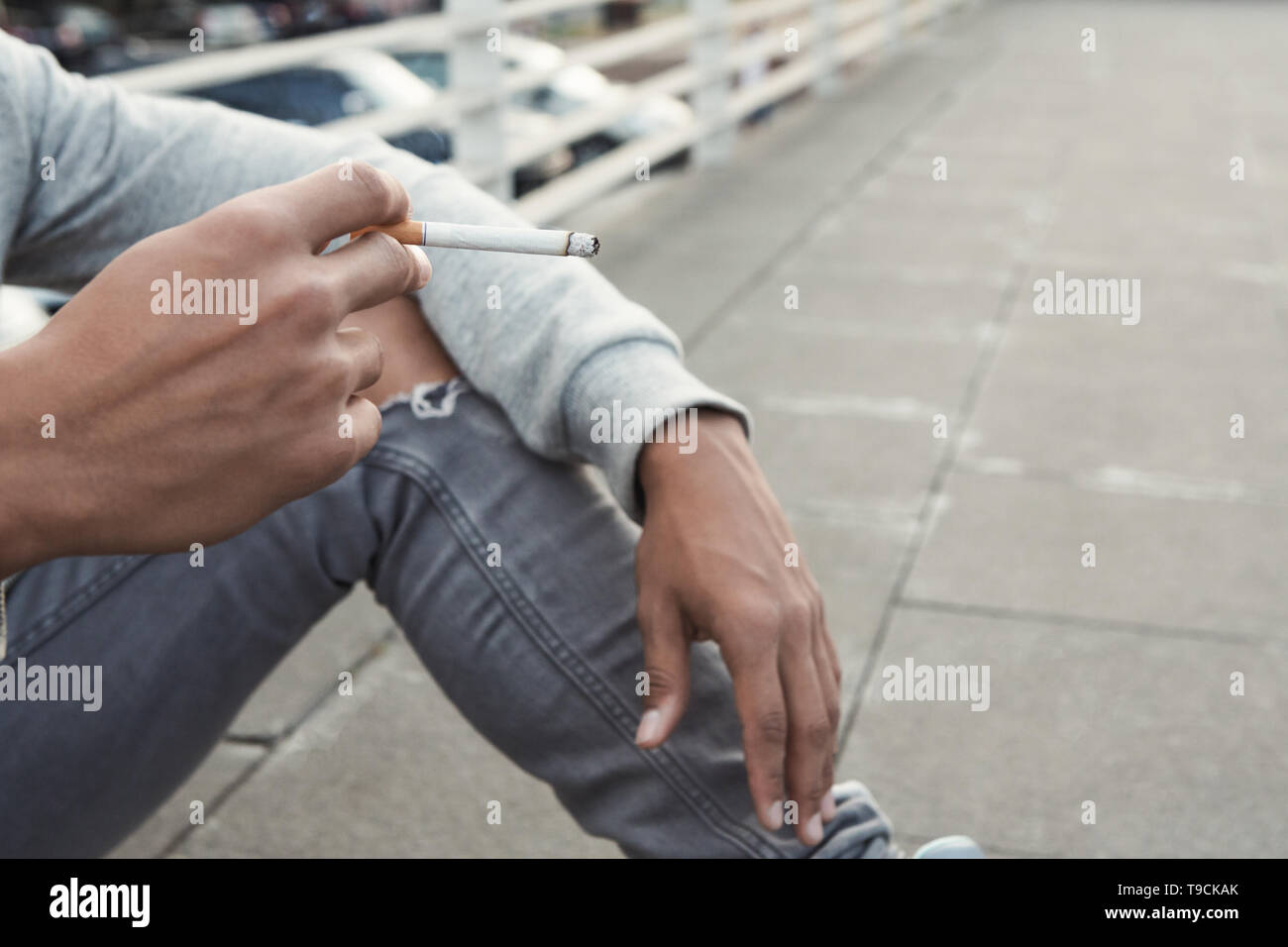 Teen Issues. Black teenager smoking cigarette, sitting alone Stock Photo