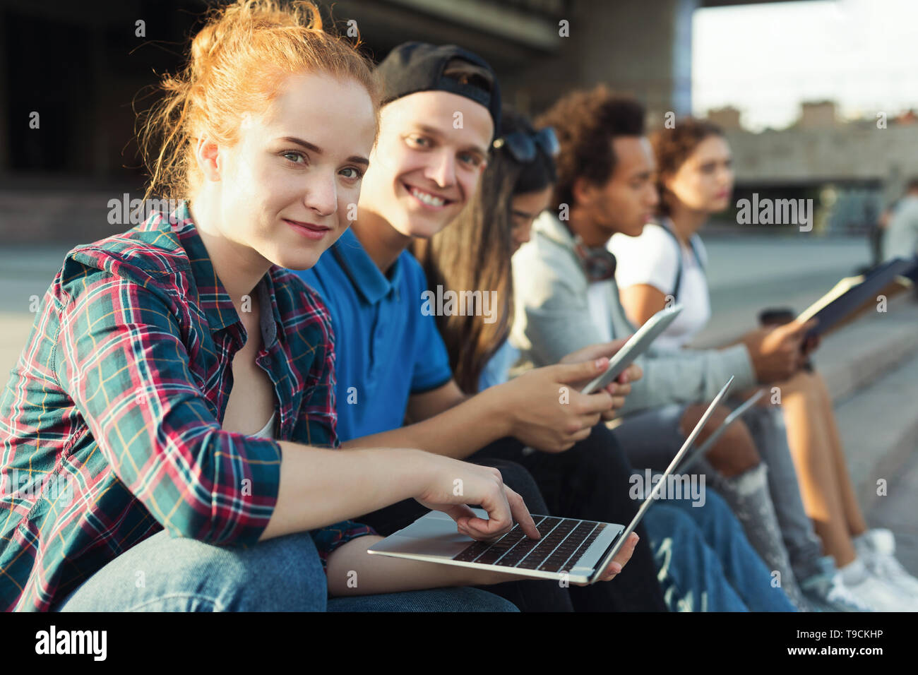 Cute redhead girl using laptop, studying with her teen friends Stock Photo