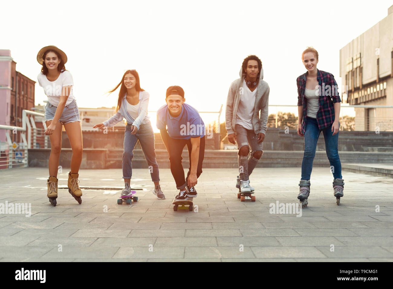 Happy teenagers having fun, riding on skateboards and rollers Stock Photo