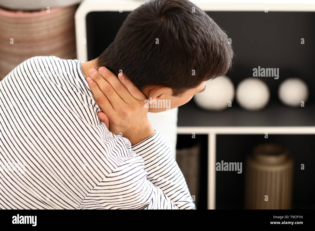 Young man suffering from neck pain at home Stock Photo - Alamy