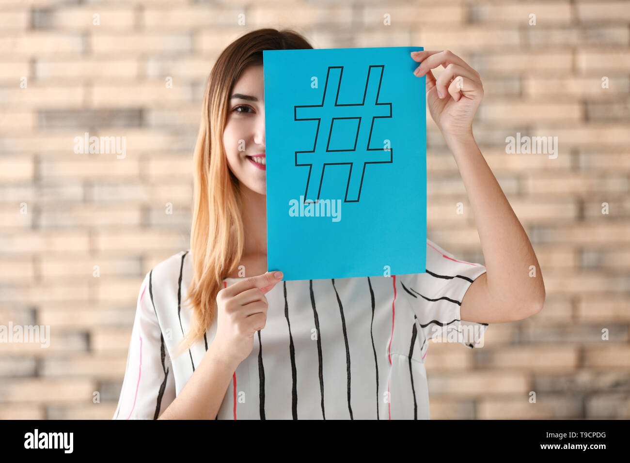 Hashtag Paper Woman holding sheet of paper with hashtag sign on brick background ...