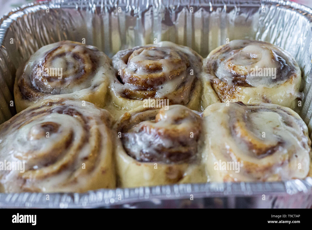 Six frosted cinnamon rolls in an aluminum foil baking pan Stock Photo