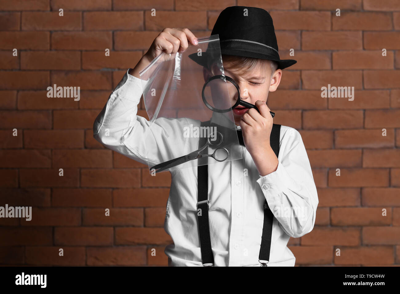 Cute little detective with evidence against brick wall Stock Photo Alamy