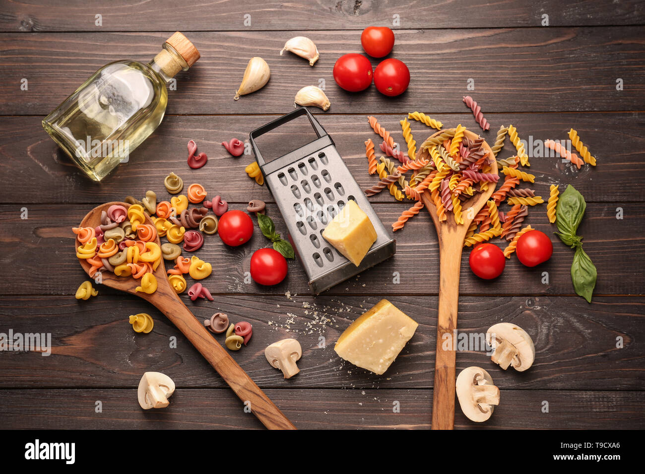 Different raw pasta with vegetables and cheese on dark wooden table Stock Photo