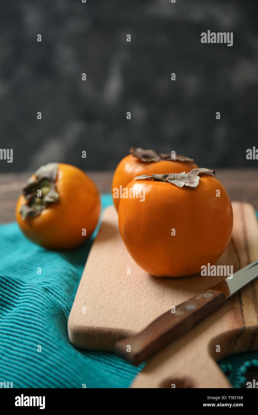 Tasty ripe persimmons with cutting board on table Stock Photo