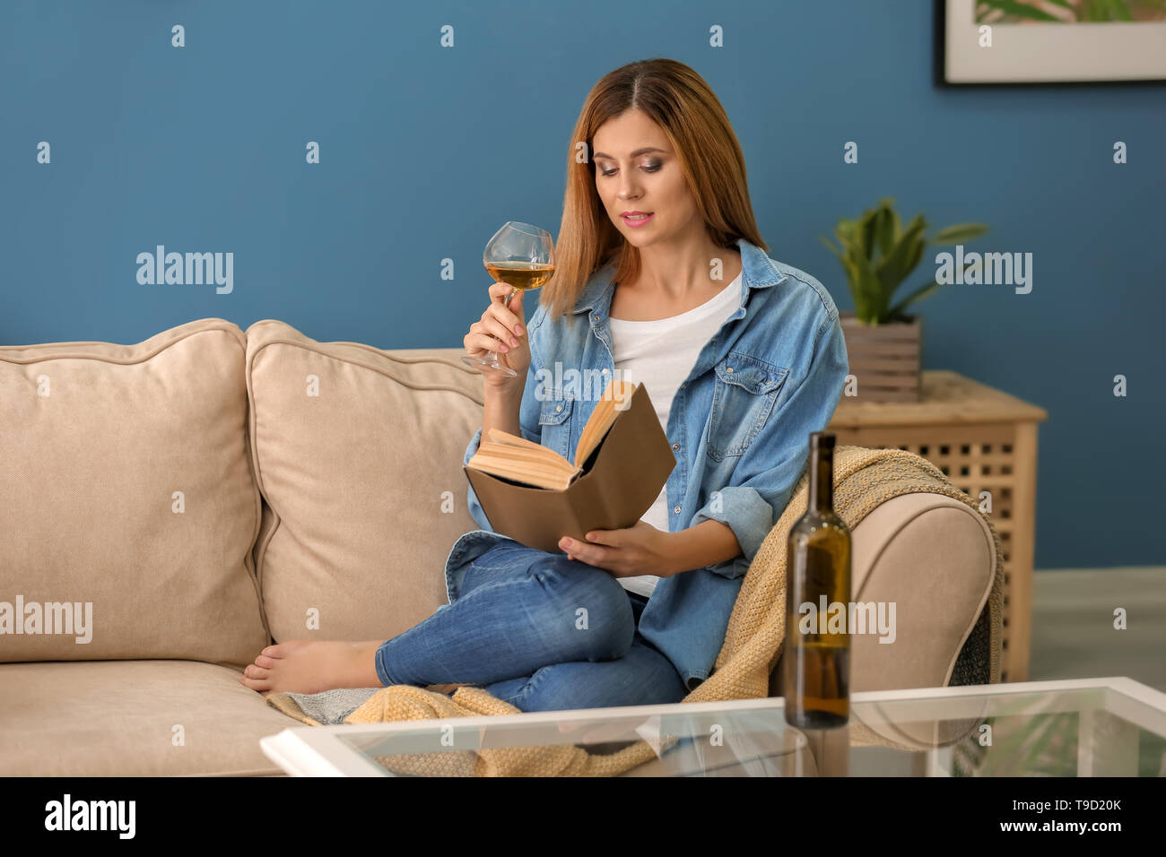 Beautiful woman with glass of wine and book on sofa at home Stock Photo ...