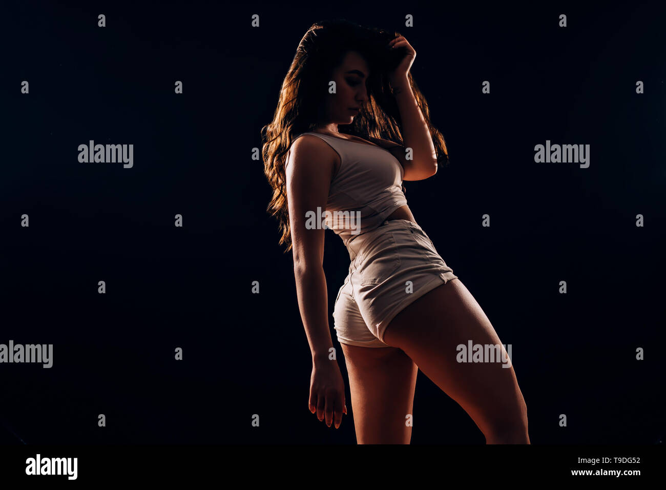 Dance, fitness, sports, health concept. Beautiful brunette woman with a slim  figure in white shorts and top posing on a black background in the dark  Stock Photo - Alamy