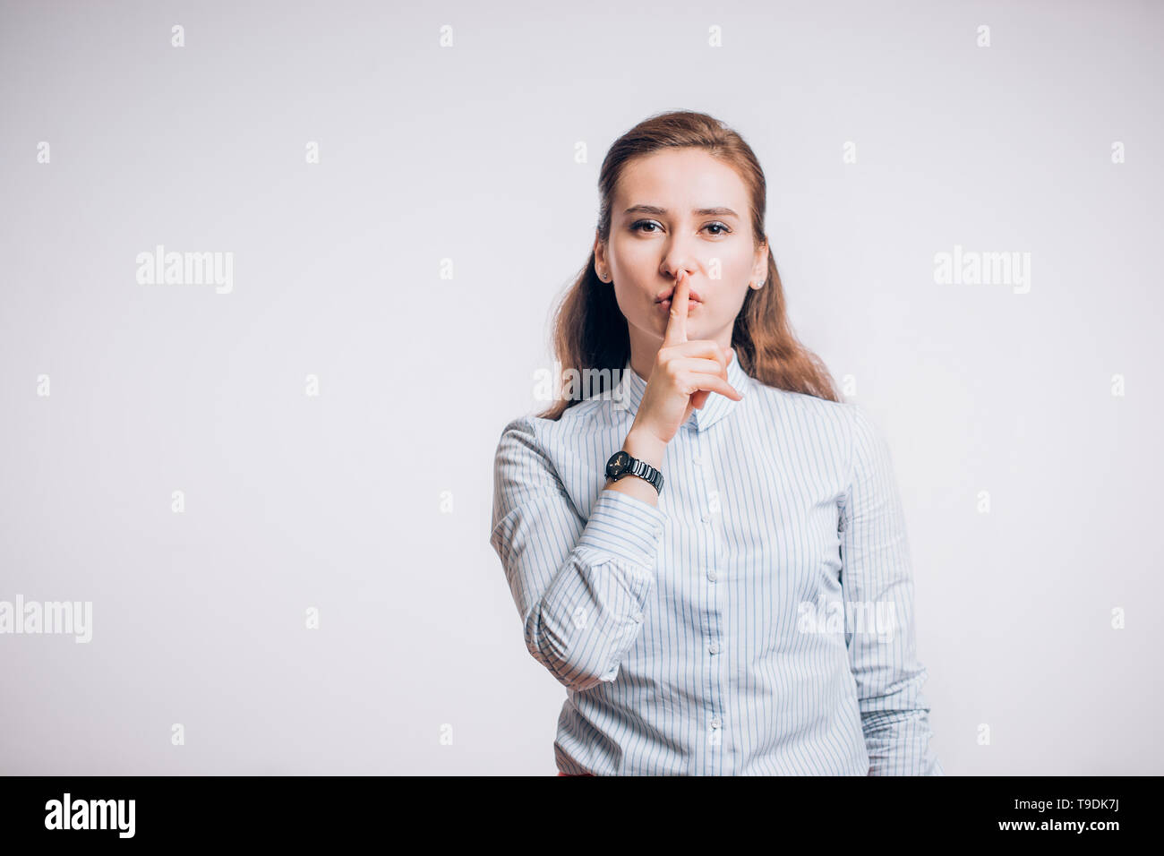 Beautiful young brunette woman keeps forefinger on lips, tells secret , demands silence on a white background with copy space Stock Photo