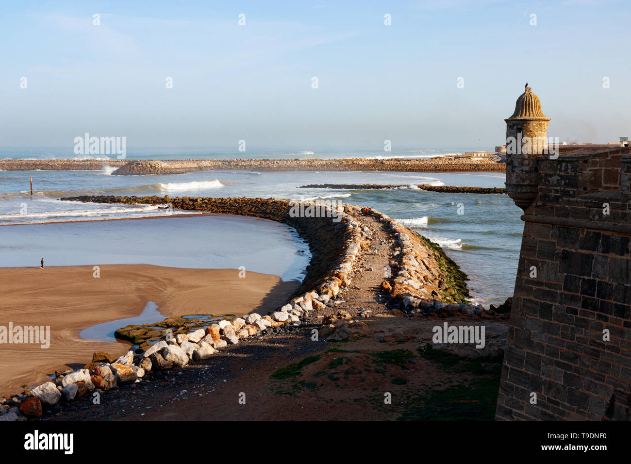 Medieval wall with small turret of Kasbah of the Udayas and an view breakwaters that separate the Bou Regreg river mouth from the Atlantic Ocean. Stock Photo
