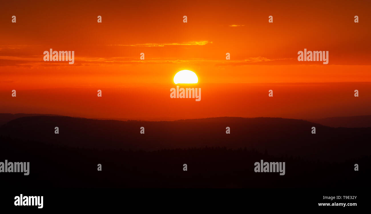 Scenic sunset over mountains. Glowing sun and orange sky and mountain range scenery or landscape. Stock Photo