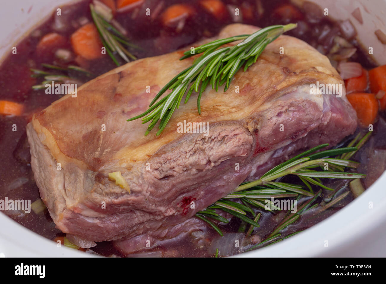 Lamb shoulder with herbs, red wine and vegetables in a casserole bowl, ready for braising. Stock Photo