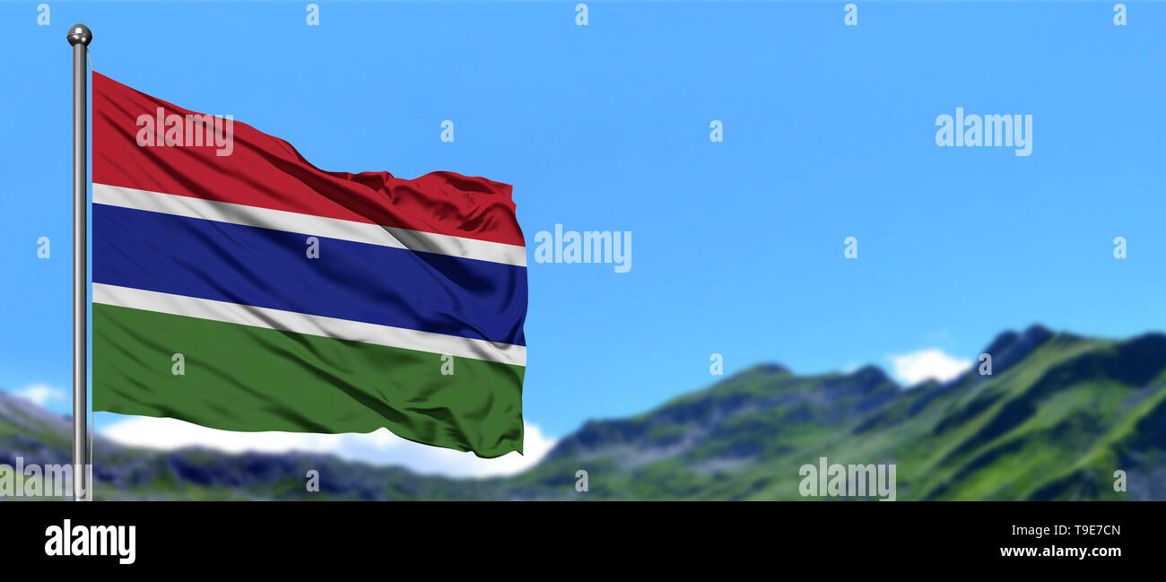 Gambia flag waving in the blue sky with green fields at mountain peak ...