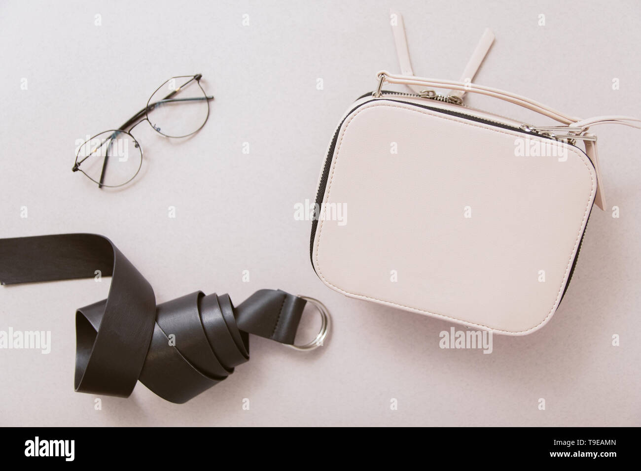 White bag, black leather belt and fashion glasses on a beige background. The concept of feminine style. Copyspace and top view Stock Photo