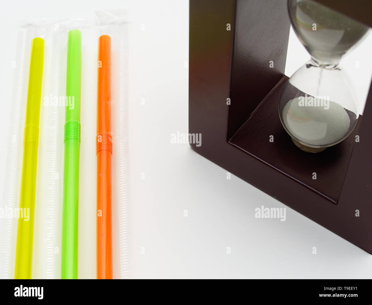 Three colored plastic straws and a hourglass. White background with