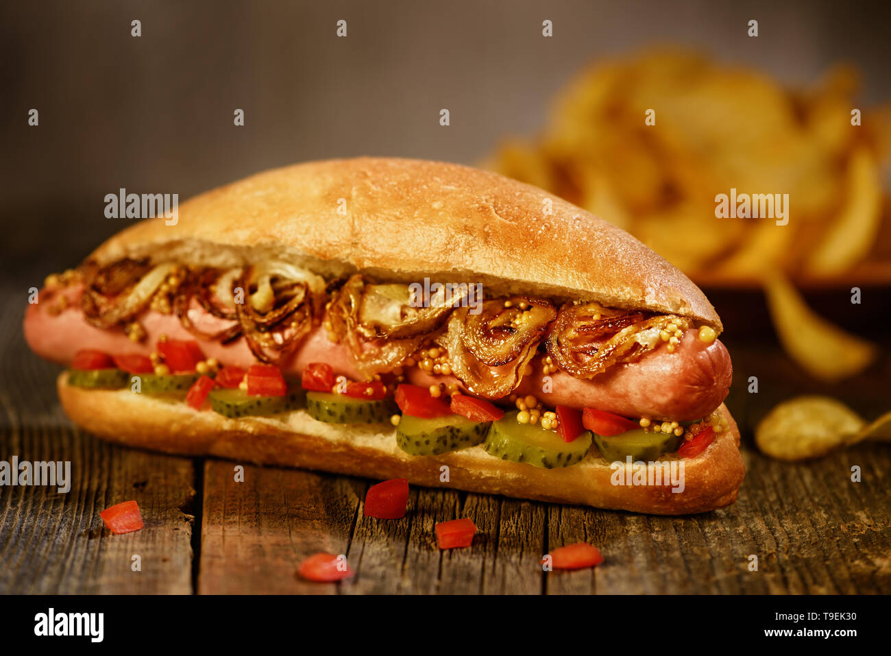 Hot dog on the background of potato chips. Dish seasoned fried onions, pickled cucumber. Stock Photo