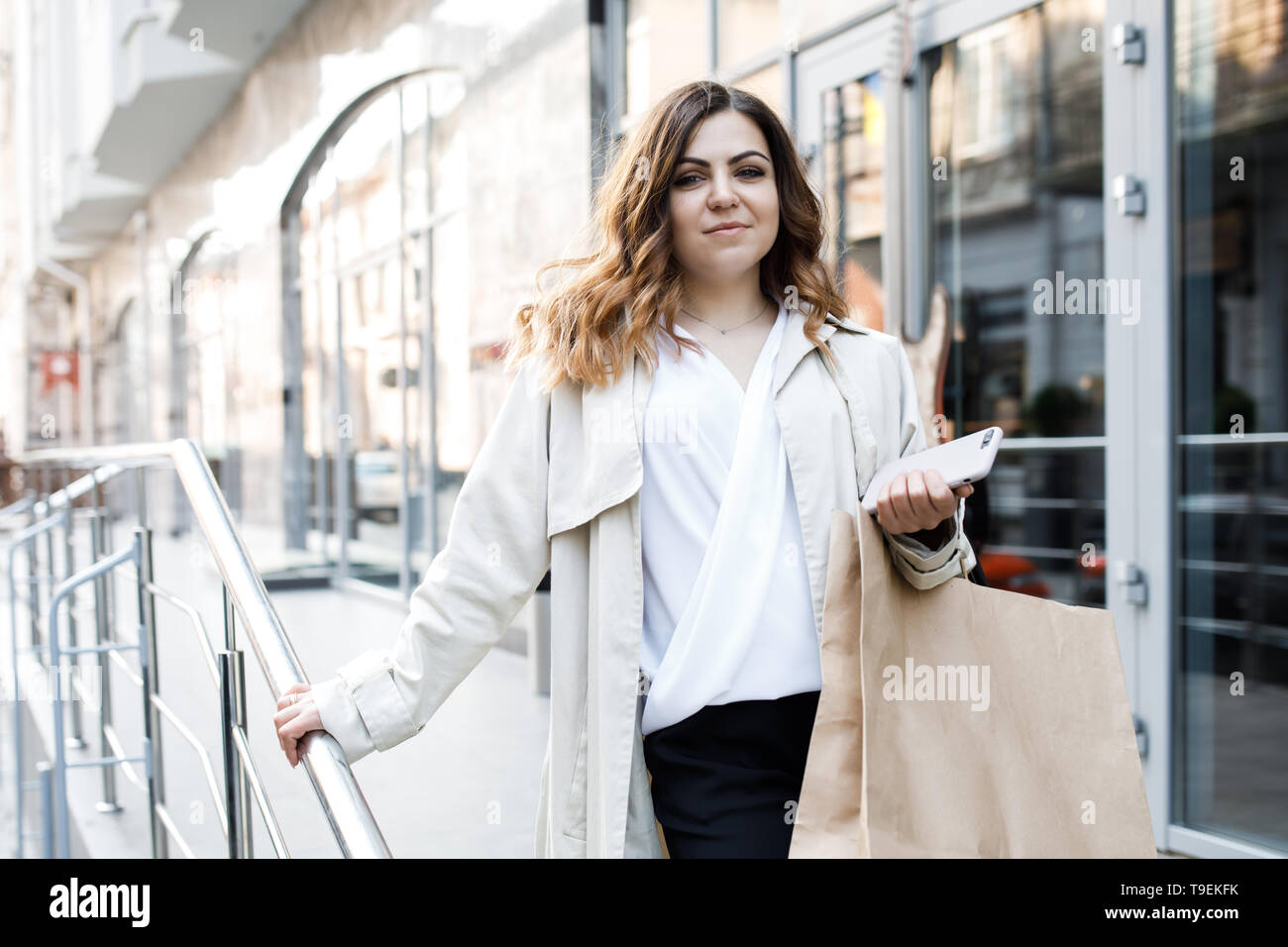 A young, sympathetic woman, not a thin-headed body building, walks around the city with a shopping bag, holds the phone in her hands and has fun. Stock Photo