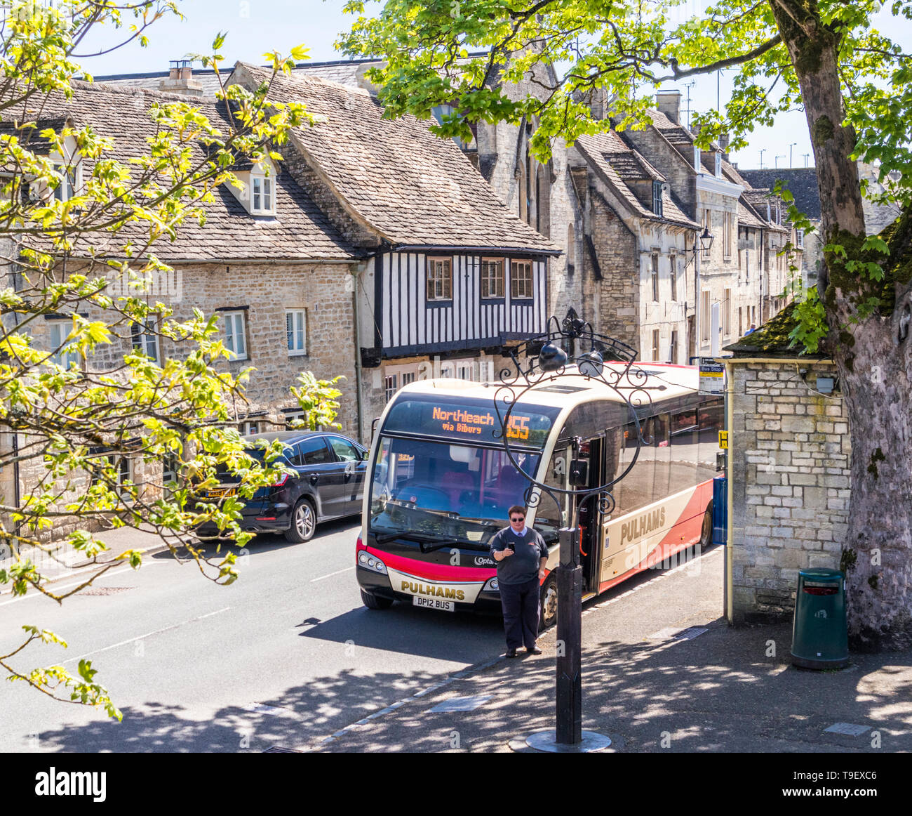A Pulhams Coaches bus waiting at a stop beside old stone houses in the Market Place in the ancient Cotswold town of Northleach, Gloucestershire UK Stock Photo
