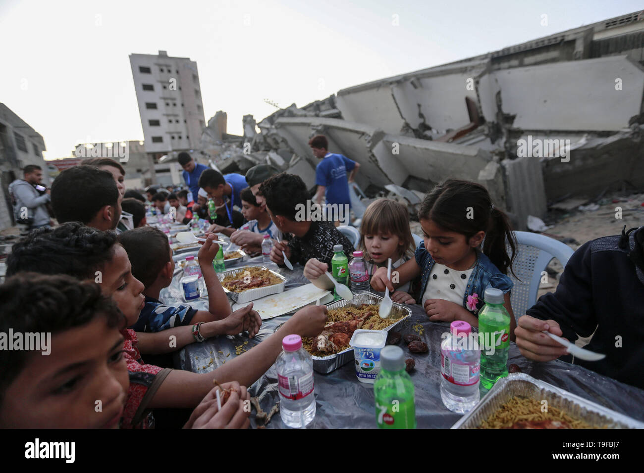 Gaza, Palestinian Territories. 19th May, 2019. Palestinian families break their fast during the Muslim holy fasting month of Ramadan, next to the remains of a building that was destroyed during Israeli air strikes. Credit: Mohammed Talatene/dpa/Alamy Live News Stock Photo
