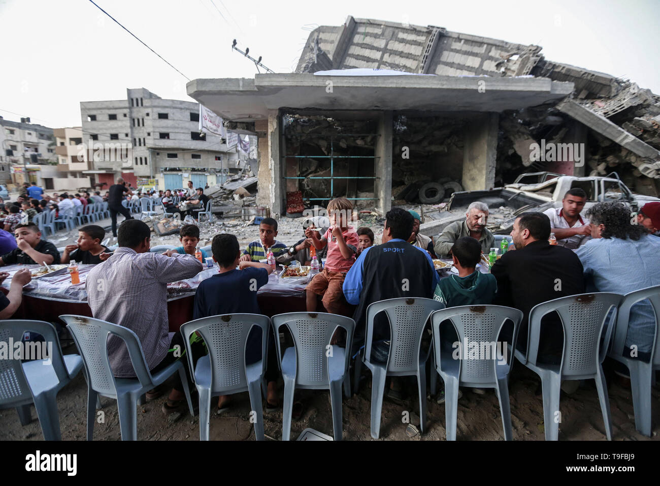 Gaza, Palestinian Territories. 19th May, 2019. Palestinian families break their fast during the Muslim holy fasting month of Ramadan, next to the remains of a building that was destroyed during Israeli air strikes. Credit: Mohammed Talatene/dpa/Alamy Live News Stock Photo